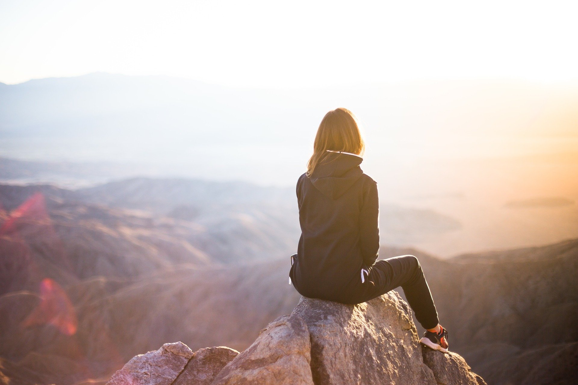 A young woman sitting on a mountain cliff gazing the early morning sun rays
