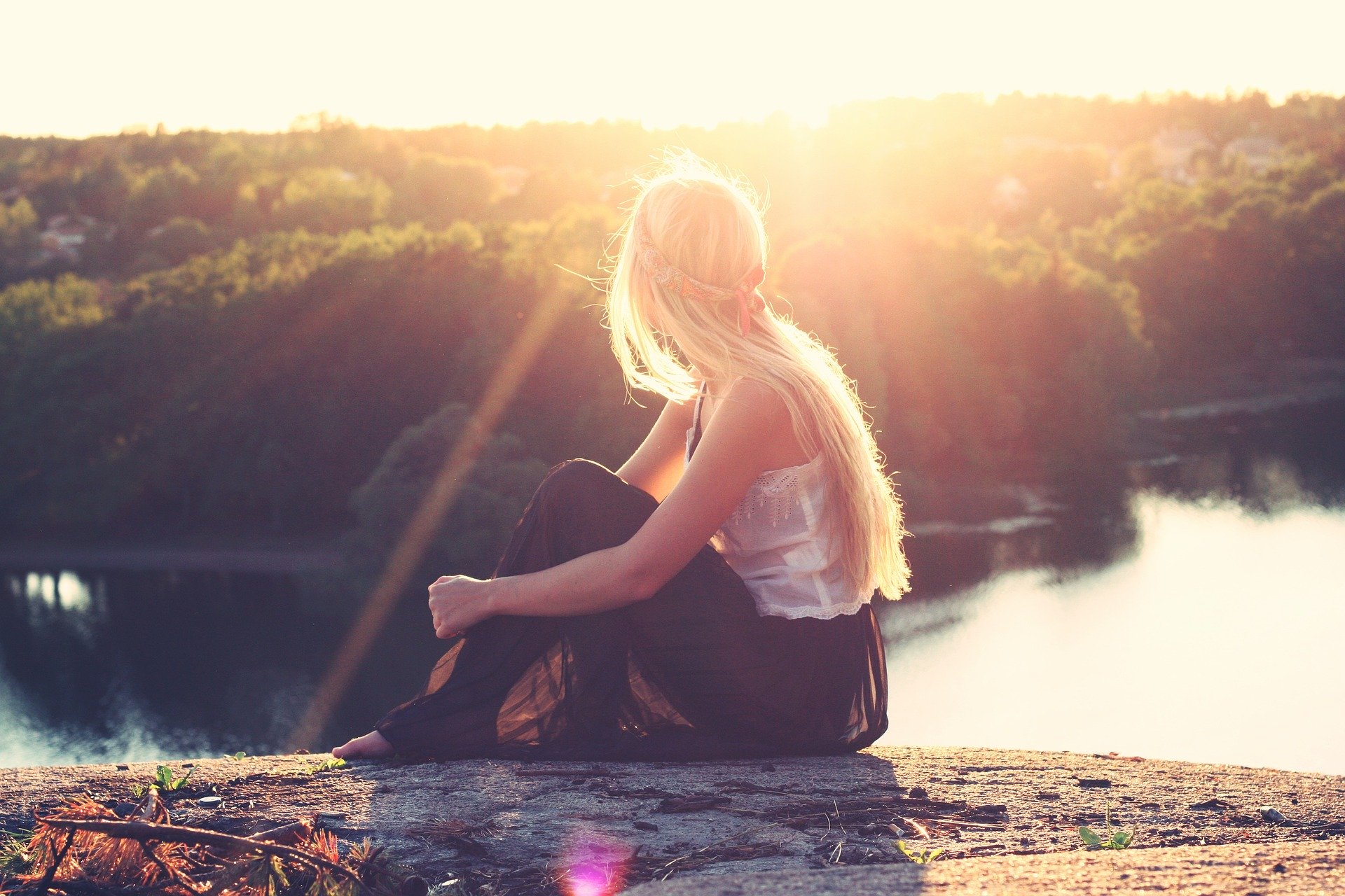 Young woman sitting on hill top watching down the river flowing 