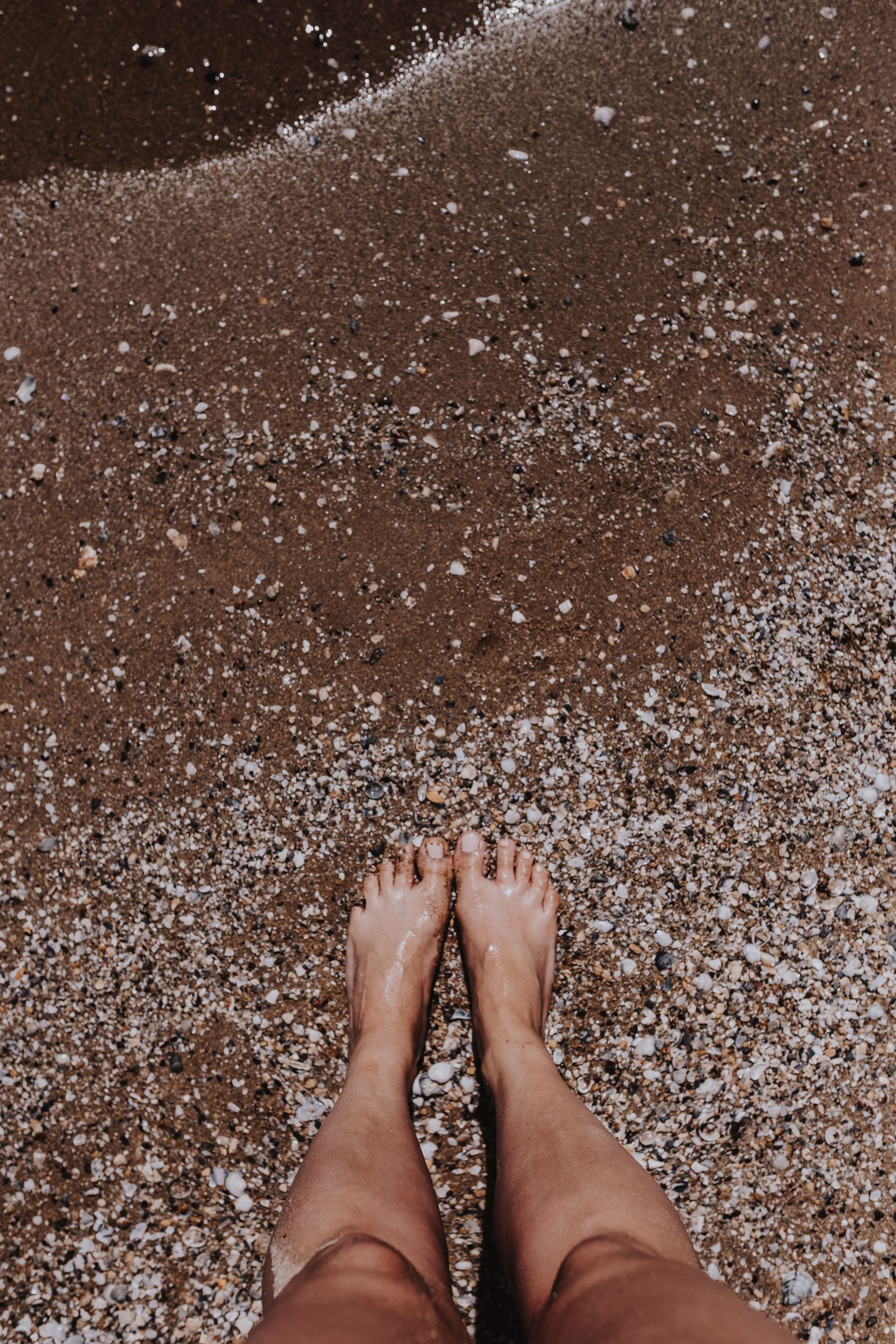 A Woman standing near sea shore with waves touching her feet